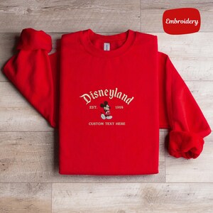 A red t-shirt with the text "Disneyland" and "EST. 1955" printed on it, along with "CUSTOM TEXT HERE" below.