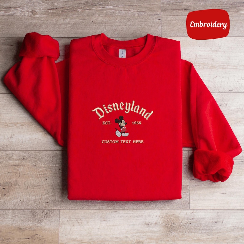A red t-shirt with the text "Disneyland" and "EST. 1955" printed on it, along with "CUSTOM TEXT HERE" below.