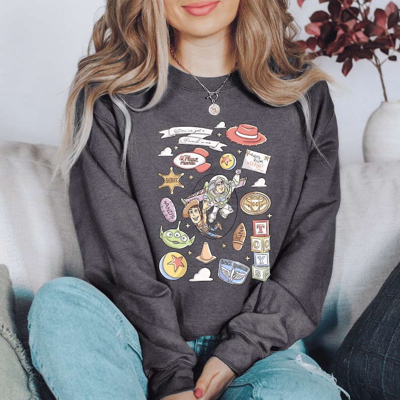A woman wearing a gray sweatshirt with a graphic design featuring various cartoon characters and icons, including a character holding a toy car.