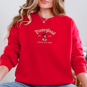 A woman wearing a red sweater with the text "Disneyland" and "EST. 1955" printed on it.