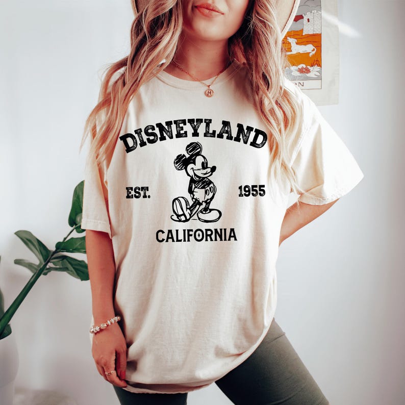 A woman wearing a white t-shirt with a graphic of Mickey Mouse and text that says "Disneyland Est. 1955 California".