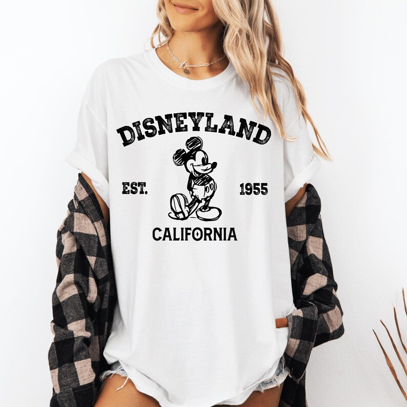 A woman wearing a white t-shirt with a graphic of Mickey Mouse and text that says "Disneyland EST. 1955 CALIFORNIA".