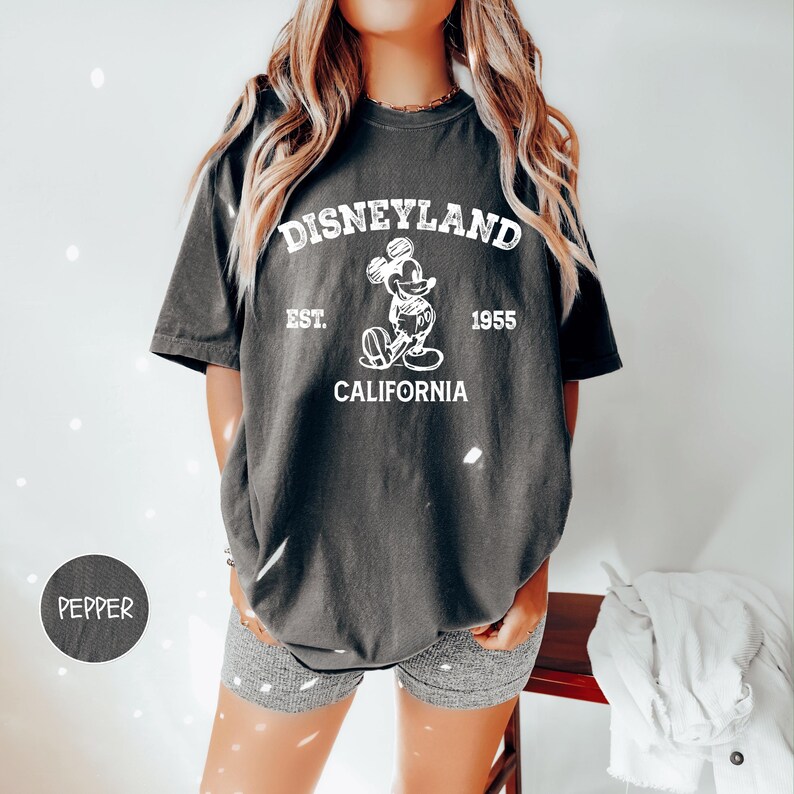 A woman wearing a black t-shirt with a Disneyland logo and text, standing in front of a white background.