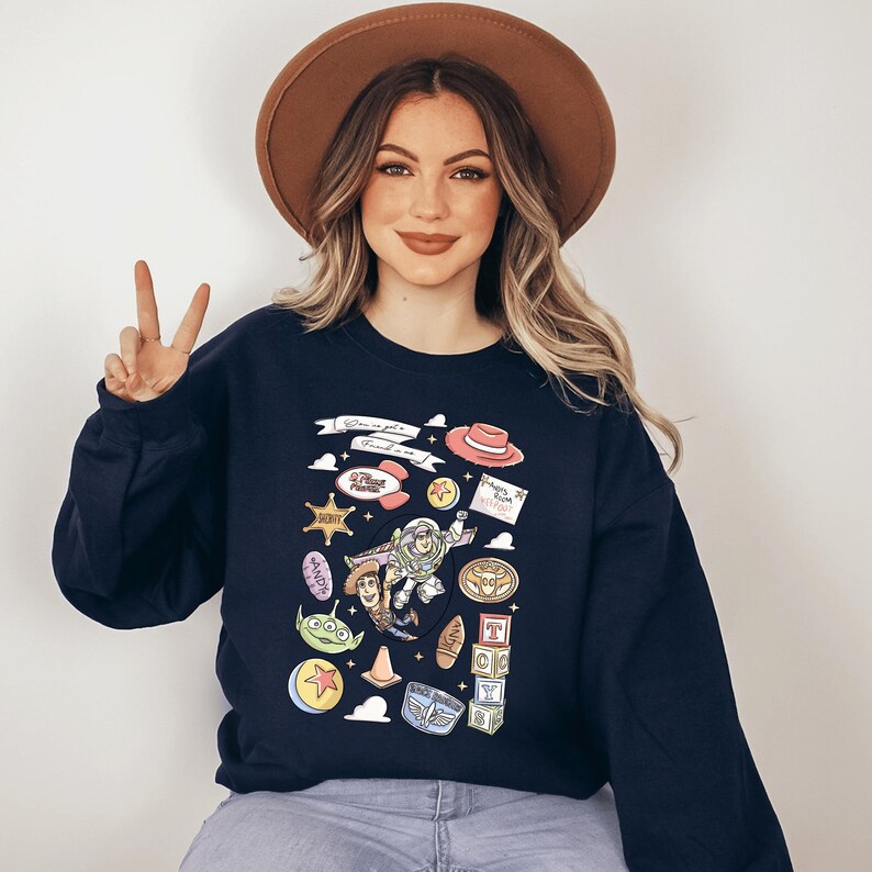 A woman wearing a black sweatshirt with a graphic design of various cartoon characters and icons, including a character holding a sign and a character holding a sign with a heart.