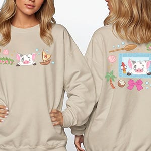 two women wearing beige sweatshirts with colorful illustrations of cartoon pig characters and various tropical elements.