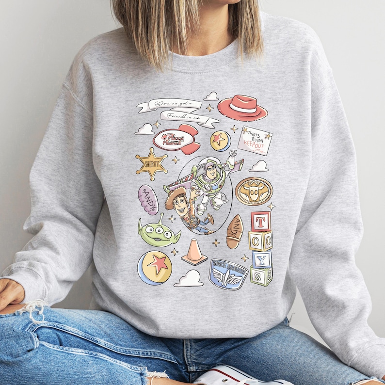 A person wearing a gray sweatshirt with a colorful graphic design featuring various characters and objects from the Toy Story franchise.