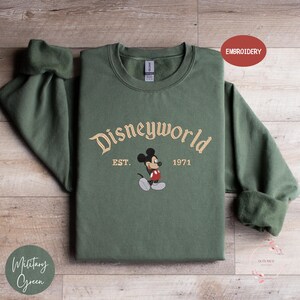 A green sweatshirt with the text "Disneyworld EST. 1971" and an embroidered image of Mickey Mouse, which appears to be a Disney-themed design.
