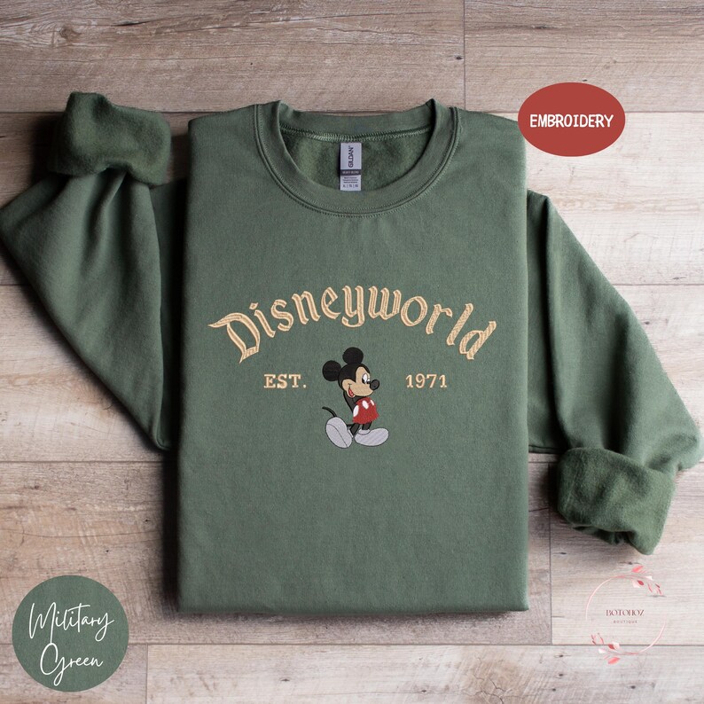 A green sweatshirt with the text "Disneyworld EST. 1971" and an embroidered image of Mickey Mouse, which appears to be a Disney-themed design.