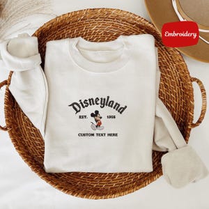 A white t-shirt with a Disney Mickey Mouse logo and text, placed in a woven basket.