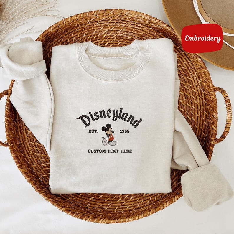 A white t-shirt with a Disney Mickey Mouse logo and text, placed in a woven basket.