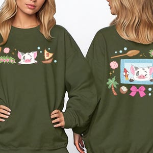 two women wearing green sweatshirts with colorful and whimsical designs, including a pig, flowers, and other decorative elements.