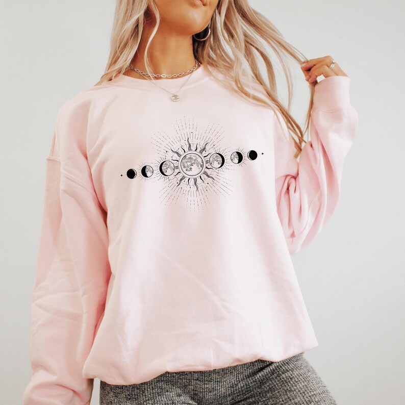 A woman wearing a pink sweatshirt with a graphic design depicting the phases of the moon.