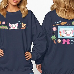 two women wearing navy blue sweatshirts with colorful cartoon pig designs and various decorative elements.
