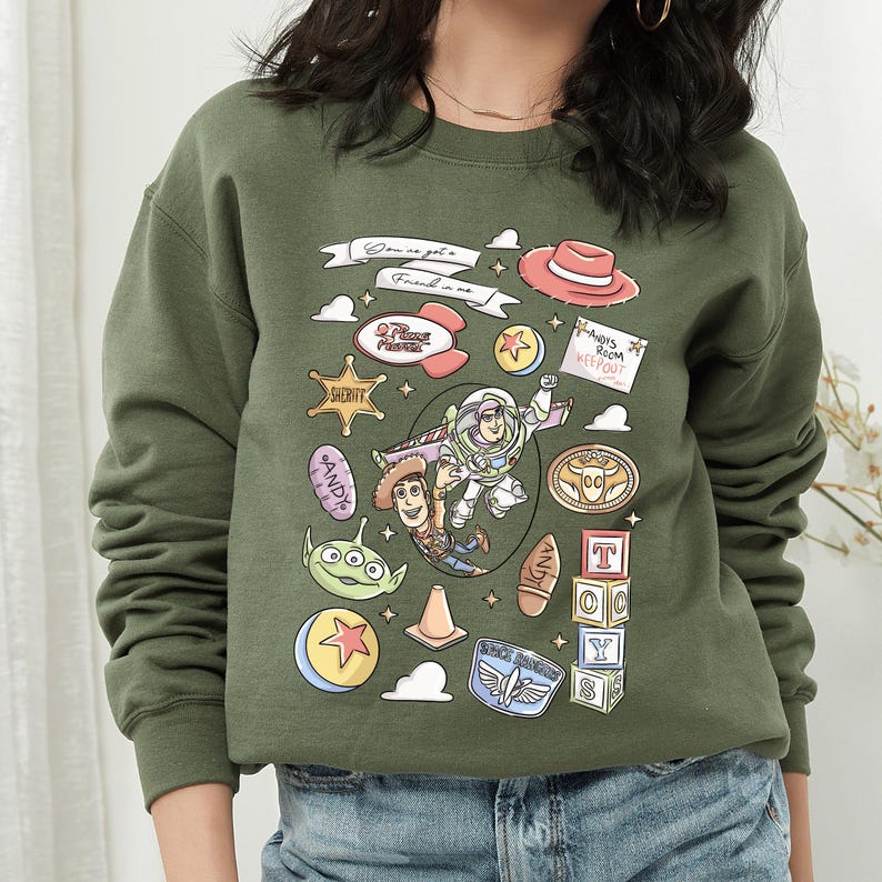 A green sweatshirt with a collage of various cartoon characters and icons, including Woody from Toy Story, Buzz Lightyear, and other iconic figures from the Toy Story franchise.