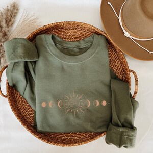 a green sweatshirt with a sun and moon design, a brown hat, and a woven basket containing a green sweater and a pair of pants.