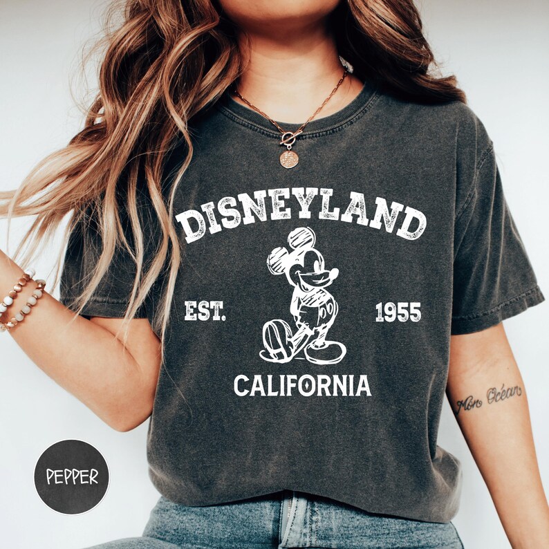 A woman wearing a black t-shirt with a graphic of Mickey Mouse and text that says "Disneyland Est. 1955 California".