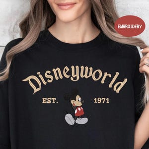 A woman wearing a black t-shirt with the text "Disneyworld EST. 1971" and an embroidered image of Mickey Mouse.