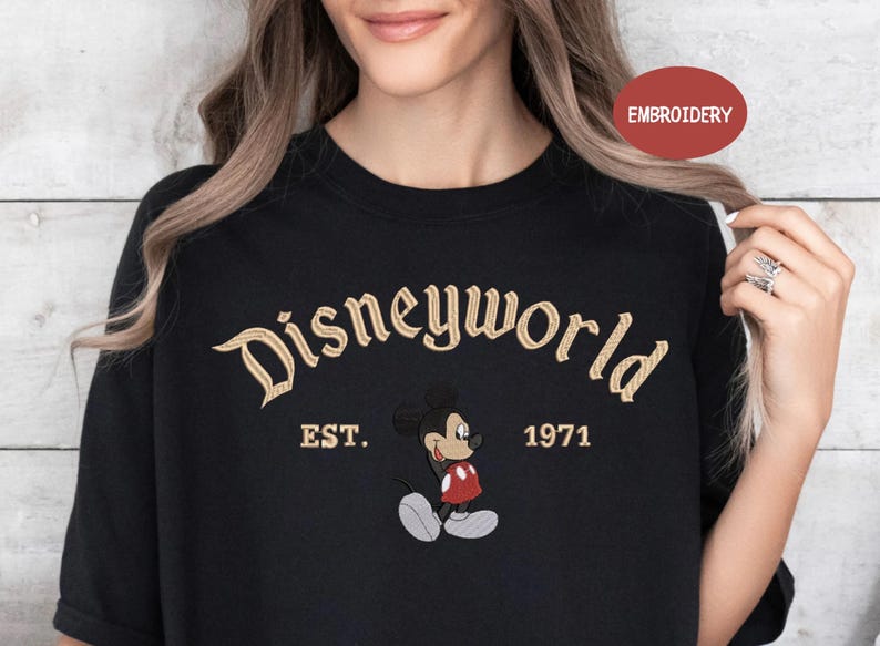 A woman wearing a black t-shirt with the text "Disneyworld EST. 1971" and an embroidered image of Mickey Mouse.