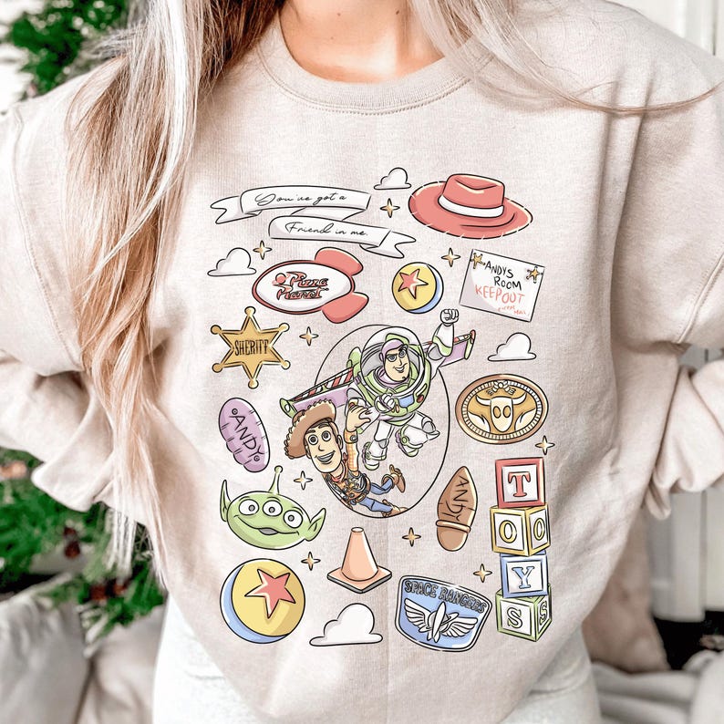 a person wearing a light-colored sweater with a collage of various cartoon characters and icons, including Woody from Toy Story, Buzz Lightyear, and other iconic characters from the Toy Story franchise.