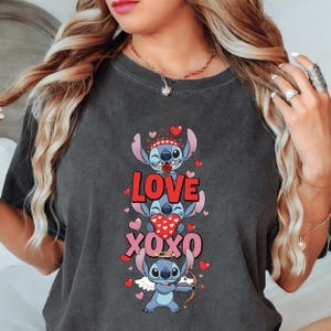 A woman wearing a gray t-shirt with a graphic design featuring a cartoon character and the text "LOVE xOXO" surrounded by hearts.