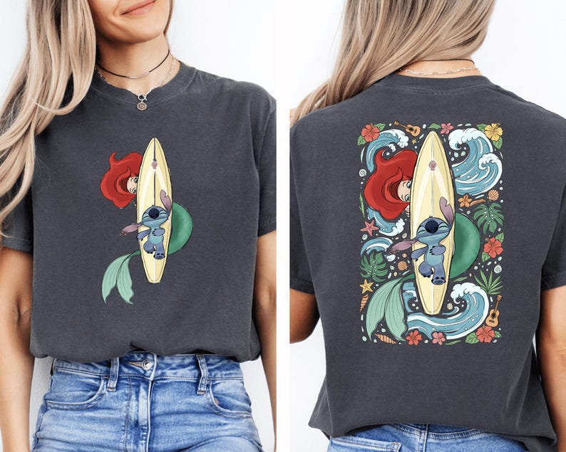a woman wearing a gray t-shirt with a colorful graphic design on the back. The design depicts a mermaid riding a surfboard, surrounded by various elements such as flowers, waves, and a starfish.