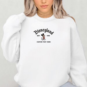 A woman wearing a white sweatshirt with the text "Disneyland" and "Est. 1959" printed on it.