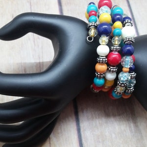 May include: A set of five colorful beaded bracelets with silver accents. The bracelets are stacked on a black hand model. The bracelets feature turquoise, red, yellow, orange, and white beads.