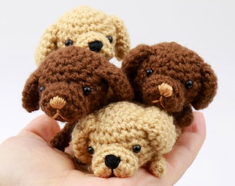 May include: Four crocheted stuffed dogs, two brown and two beige, are piled on top of each other in a hand. The dogs have black eyes and brown noses.