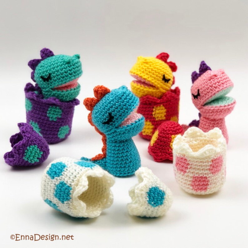 May include: Four crocheted dinosaur toys in different colors, each with a crocheted egg. The dinosaurs are turquoise, pink, yellow, and purple. The eggs are white with blue polka dots.