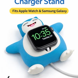 May include: A blue and white Apple Watch charger stand in the shape of a cartoon character, holding a black Apple Watch showing the time. The stand also fits Samsung Galaxy watches. Text on the stand reads "Apple Watch Charger Stand".