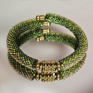 May include: Two green and gold beaded bracelets with a gold bead accent. The bracelets are made of small, round beads and have a subtle ombre effect.