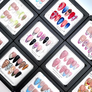 May include: A collection of press-on nails in various designs, displayed in individual black boxes. Designs include floral, plaid, animal print, and solid colors with embellishments. The text "handmade pass on nails" is visible.