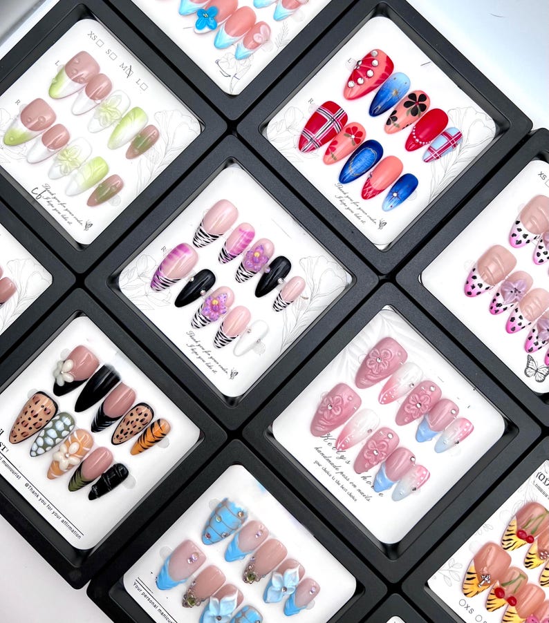 May include: A collection of press-on nails in various designs, displayed in individual black boxes. Designs include floral, plaid, animal print, and solid colors with embellishments. The text "handmade pass on nails" is visible.