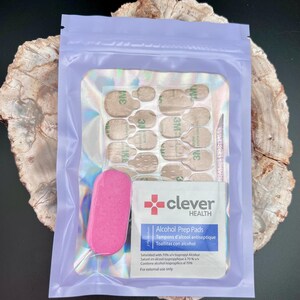 May include: A nail kit in a lavender pouch. The kit includes nail adhesive tabs, a pink nail file, a cuticle pusher, and an alcohol prep pad. The prep pad is labeled "clever HEALTH" and includes the text "Alcohol Prep Pads".