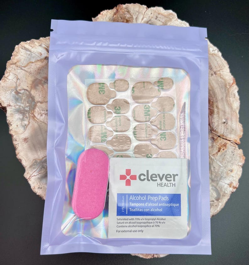 May include: A nail kit in a lavender pouch. The kit includes nail adhesive tabs, a pink nail file, a cuticle pusher, and an alcohol prep pad. The prep pad is labeled "clever HEALTH" and includes the text "Alcohol Prep Pads".