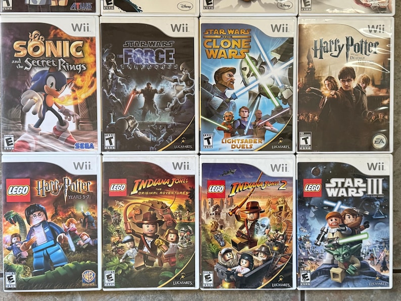 May include: A collection of Wii video game cases featuring titles like "Sonic and the Secret Rings," "Star Wars: The Force Unleashed," "Harry Potter," and Lego-themed games. The cases display colorful graphics and game titles.
