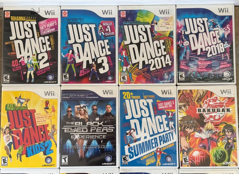 May include: A collection of Wii video game cases featuring the "Just Dance" series, including "Just Dance 2," "Just Dance 3," "Just Dance 2014," and "Just Dance 2018." Other titles include "Just Dance Kids 2," "The Black Eyed Peas Experience," and "Bakugan."