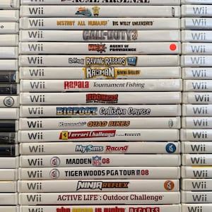 May include: A stack of Wii game cases, featuring titles like "Bakugan," "Cars Race-O-Rama," "Acme Arsenal," "Call of Duty 3," and "Madden NFL 08." The cases are white with game titles and logos.