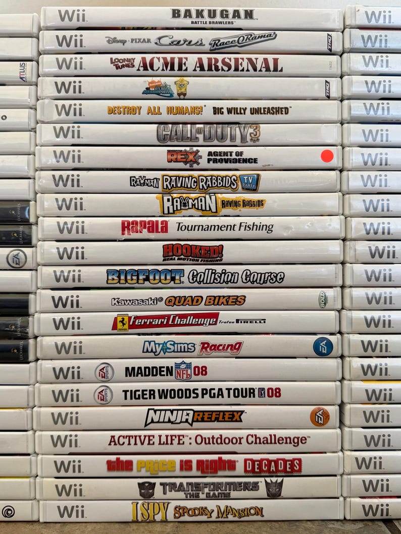 May include: A stack of Wii game cases, featuring titles like "Bakugan," "Cars Race-O-Rama," "Acme Arsenal," "Call of Duty 3," and "Madden NFL 08." The cases are white with game titles and logos.