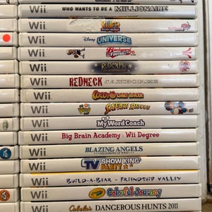 May include: A stack of Wii video game cases, featuring titles like "Super Paper Mario," "Family Feud," and "Jeopardy!" The cases are white with colorful game art and text, showcasing a variety of game genres.