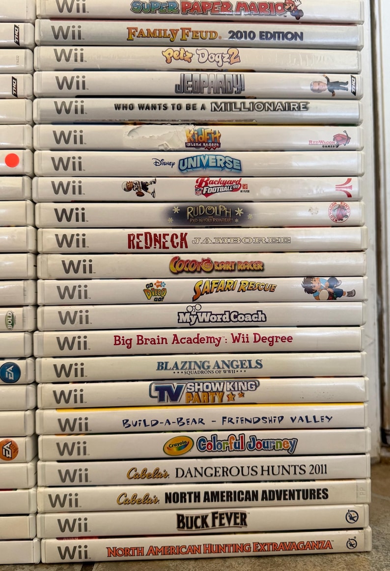 May include: A stack of Wii video game cases, featuring titles like "Super Paper Mario," "Family Feud," and "Jeopardy!" The cases are white with colorful game art and text, showcasing a variety of game genres.