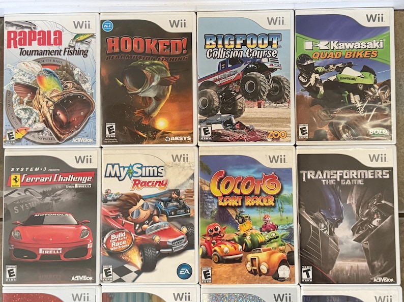 May include: A collection of Wii game cases. Titles include "Rapala Tournament Fishing", "Hooked! Real Motion Fishing", "Bigfoot Collision Course", "Kawasaki Quad Bikes", "Ferrari Challenge", "My Sims Racing", "Cocoto Kart Racer", and "Transformers: The Game".