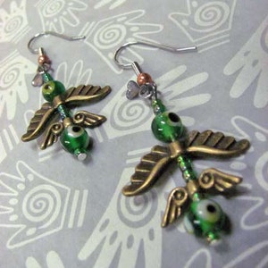 May include: A pair of green and gold earrings with a winged design. The earrings feature green glass beads with black centers and gold metal wings.