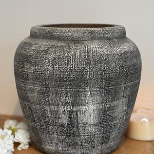 May include: A large, round, black and white ceramic planter with a textured surface. The planter is sitting on a wooden surface.