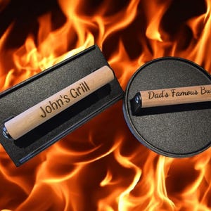 Op de afbeelding: Twee gietijzeren grillpersen met houten handvatten. De bovenste pers heeft de tekst "John's Grill" gegraveerd op het handvat. De onderste pers heeft de tekst "Dad's Famous Burgers" gegraveerd op het handvat.