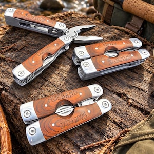 May include: Three multi-tools with silver metal frames and wood grain handle inlays. One tool is open, showing pliers. The handles are engraved with the names Daniel, Harry, and the word HUSBAND, along with the dates 24.09.2025 and 27.09.2025.