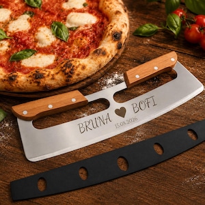 Może przedstawiać: Nóż do pizzy ze stali nierdzewnej z dwoma drewnianymi uchwytami i czarną osłoną ostrza. Metalowe ostrze jest wygrawerowane napisem BRUNA, symbolem serca, BOFI oraz datą 15.08.2026, umieszczone obok pizzy i świeżej bazylii.
