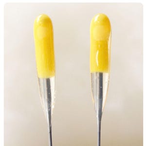 May include: Two yellow glass vials with clear liquid inside and silver needles attached to the bottom.