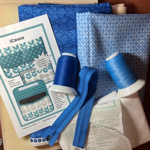 Puede incluir: Un conjunto de recortes de tela azul y blanca, dos carretes de hilo azul y una cremallera azul para un proyecto de costura DIY. La imagen incluye instrucciones para hacer una funda de teléfono con bolsillos con cremallera. Las instrucciones incluyen el texto "iCases" y "Patterns by Annie".