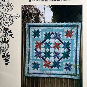 Puede incluir: Un patrón de colcha titulado "Quarters Quilt" de la colchadora Mary Jane Best. La colcha está hecha de tela azul, roja y morada y presenta un patrón de estrellas. La colcha está colgada en una valla de madera.
